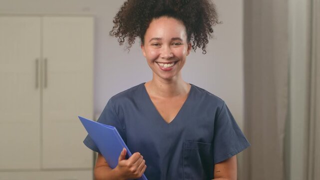 Friendly Black Woman Doctor With Natural Hair And Scrubs Smiles Confidently