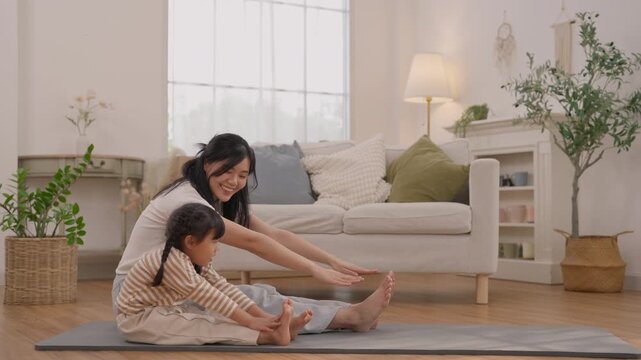 Mother and daughter stretching on yoga mat in bright living room, woman and child sitting together with gentle smiles, family wellness, indoor plants, healthy lifestyle and comfortable home decor