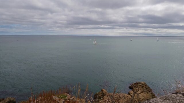 Sailboats participating in the Tri-Coastal Race Series final leg navigate the ocean waters near Fowey, Cornwall. The view is from St Catherine's Castle, overlooking the seascape and cloudy sky.