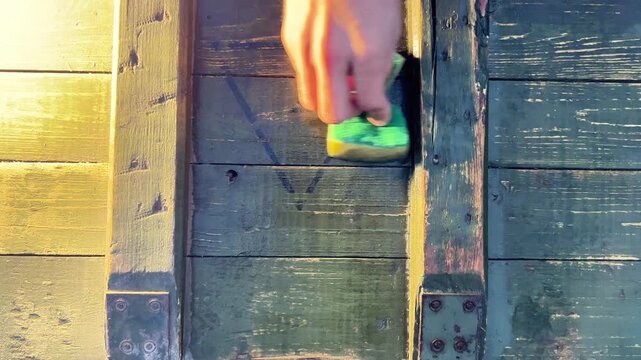 Top view close up shot of a hand scrubbing dirt and marks off a green wooden military box using a sponge outdoors. Restoration concept.