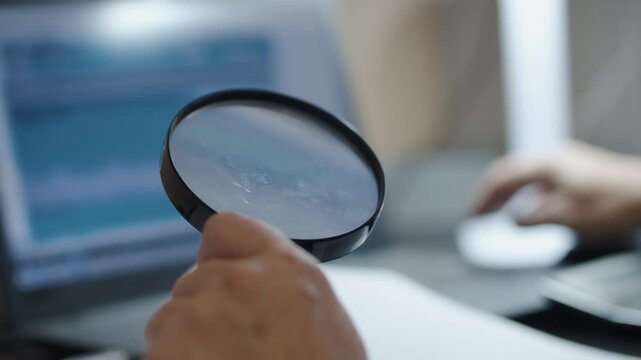 Magnifying Glass Inspecting Document Beside Laptop in Office