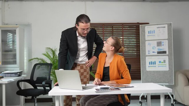 Male manager inappropriately touching female subordinate's shoulder while discussing work on a laptop, leading to discomfort, rejection, and office harassment