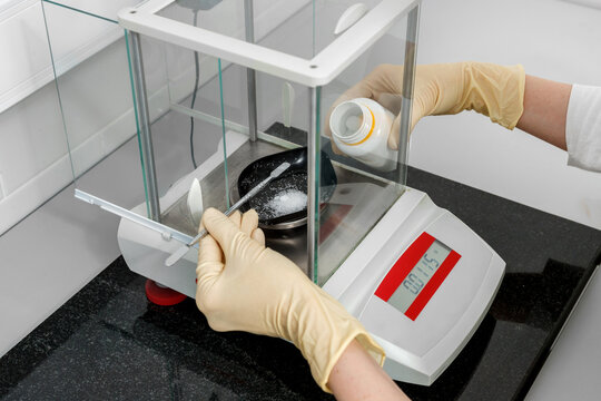 Specialist in gloves weighing a reagent on an analytical balance in a laboratory.