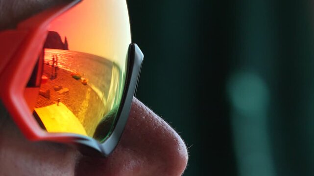 Sunset beach reflection glowing in colorful sports sunglasses on a person face during vacation. Extreme close-up shot.