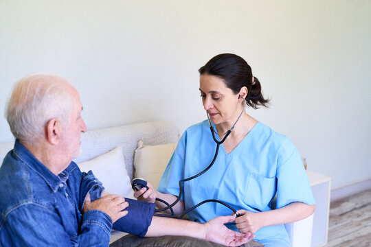 Home healthcare and senior care, nurse checking elderly man's blood pressure during a house call in a bright living room