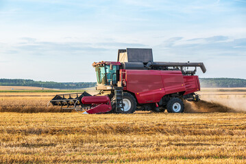 Obraz premium Red combine harvester working in golden wheat field under sky