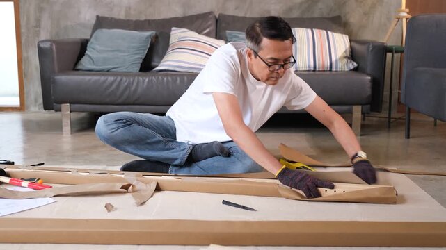 Furniture assembly man unpacking cardboard with tool in living room beside sofa building flat pack table frame at home