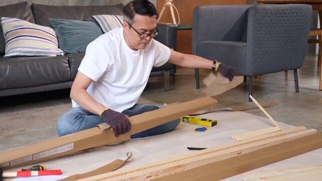 Adult man furniture assembly in living room with cardboard, wood tool, sofa scene, flat pack table on floor indoors