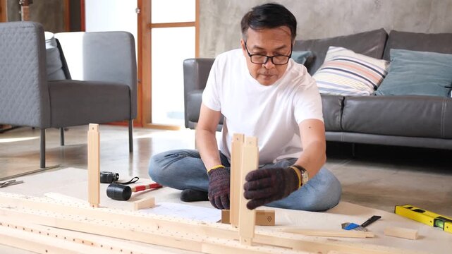 senior Man furniture assembly wood home tool scene focused adult building wooden frame on living room floor near sofa