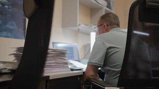 Office Worker Working at Computer With Stack of Documents