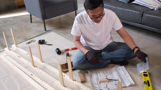 Furniture assembly man using instruction guide and tool for wood home project building flat pack shelf on floor