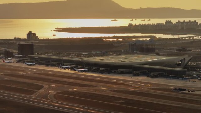 Aerial view of Navi Mumbai International Airport during sunset, showcasing the modern terminal, runways, surrounding waterways, and urban landscape of Navi Mumbai.