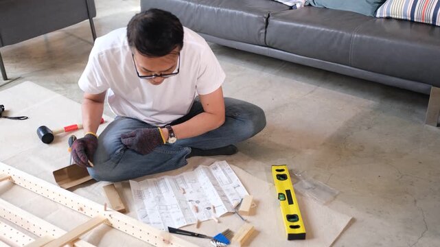 Furniture assembly man uses tool and instruction level in living room building wood frame on floor for home project