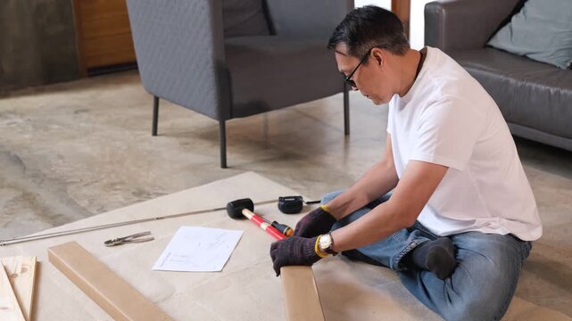 Furniture assembly Adult man uses tool on wood plank for home repair, focused floor work near sofa in living room