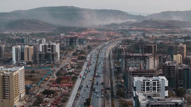 Aerial view of the Uran Panvel Road corridor near Navi Mumbai, showcasing a busy highway, modern urban development, high-rise buildings, ongoing construction, and scenic hills in the background.
