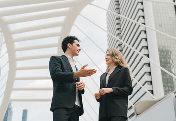 Fototapeta premium Businessman explaining with hand gesture to businesswoman on a modern skybridge with city skyscrapers, business discussion, presentation and corporate collaboration.