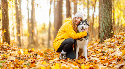 Woman in bright raincoat is having fun with her dog in an autumn park. Young woman enjoys autumn in park, walking husky outdoors. Concept of friendship, animals, and walking. Lifestyle. © maxbelchenko