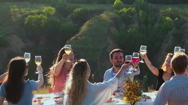 Young friends talking around decorated table in green meadow. Concept of social connection, outdoor hospitality, weekend leisure and event catering.