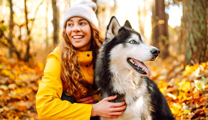 Woman in bright raincoat is having fun with her dog in an autumn park. Young woman enjoys autumn in park, walking husky outdoors. Concept of friendship, animals, and walking. Lifestyle. © maxbelchenko