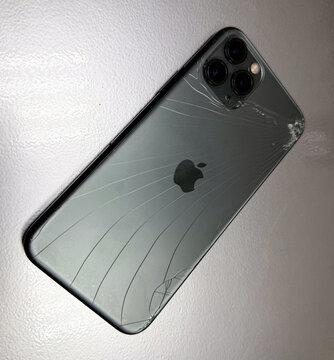 Vertical view of damaged Apple iPhone 11 Pro with smashed back glass on table, mobile phone with broken body casing and triple camera lens requiring repair, smartphone screen insurance and concept. 