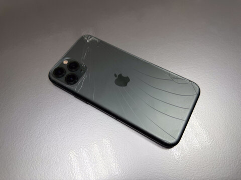 Broken Apple iPhone 11 Pro smartphone with cracked back glass panel on desk close up, damaged triple camera mobile phone casing needing repair, service center workshop concept, editorial stock photo.