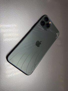 Vertical view of damaged Apple iPhone 11 Pro with smashed back glass on table, mobile phone with broken body casing and triple camera lens requiring repair, smartphone screen insurance and concept. 