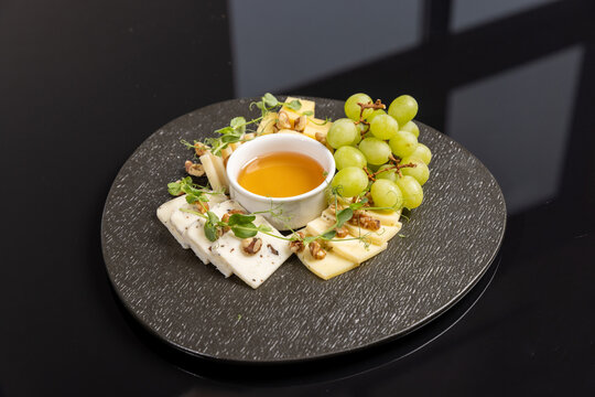 Cheese platter served with honey green grapes walnuts and microgreens on dark plate