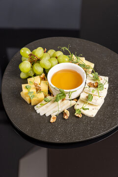 Gourmet cheese board with honey grapes and walnuts served on dark platter