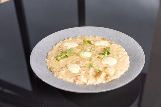 Creamy mushroom risotto topped with sauce and microgreens on grey plate