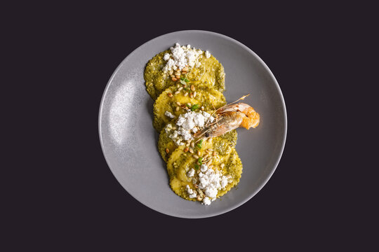 Gourmet ravioli pasta with pesto sauce, pine nuts, goat cheese, and fried shrimp served on a ceramic plate
