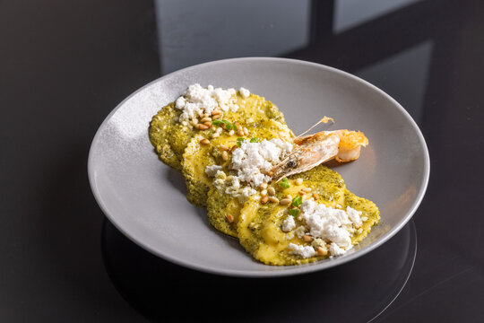 Ravioli pasta with pesto sauce feta cheese and shrimp on grey plate