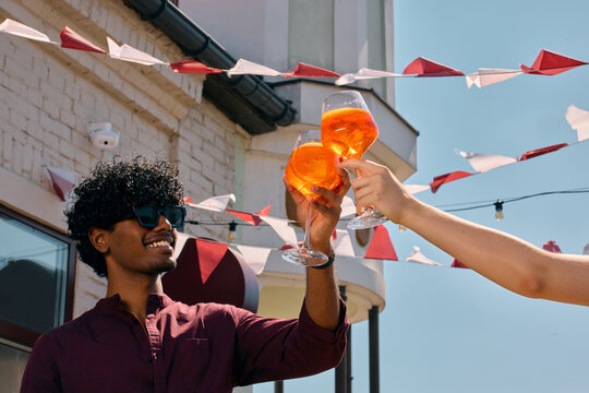 Young man toasting beer and cocktails with friends at outdoor party. Concept of social confidence, friendship, summer celebration, positive emotions and beverage campaigns.