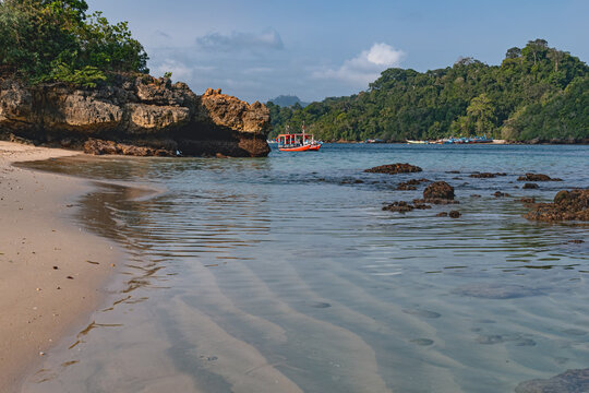 Scenic Tiga Warna Beach in Malang, East Java, Indonesia, featuring clean sandy shores, calm blue seawater, small islands and dramatic coastal cliffs surrounded by pristine tropical nature