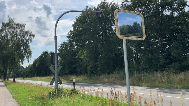 Convex traffic safety mirror beside rural road and railway crossing infrastructure