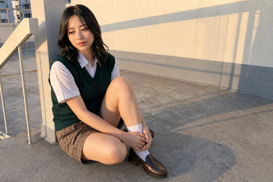 屋上で座る白シャツと緑ベストの女性