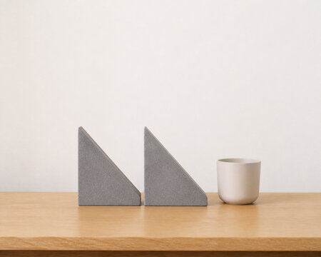 Two identical triangular bookends in row on oak desk with ceramic cup, minimalist desk organization concept