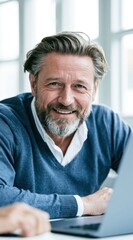 Fototapeta premium Middle-aged man with salt-and-pepper hair smiles warmly while working on a laptop in a bright indoor setting