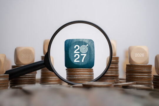 Goals in 2027: Financial Concept with Trend Analysis for 2027, Planning, and Investment - Magnifying Glass Focusing on 2027 Business Target with Coin Stacks Background.
