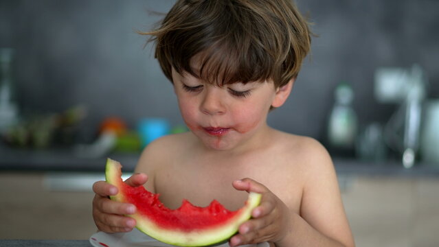 Young boy enjoys juicy watermelon slice at home, encouraging healthy eating, fresh summer nutrition and authentic childhood independence