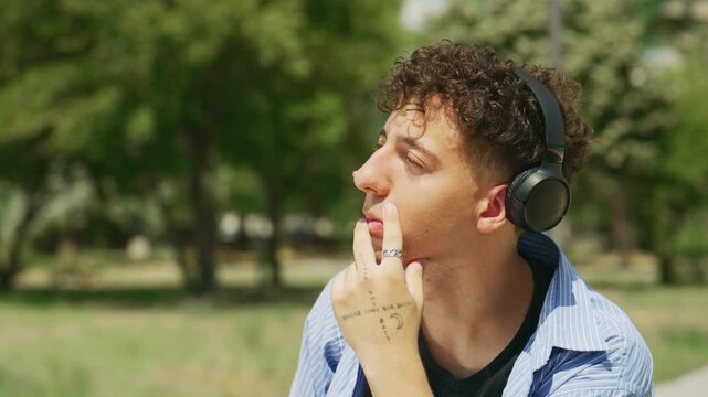 A young man is concentrating on his studies outdoors, wearing headphones and writing in a notebook. He appears focused and absorbed in his work in the fresh air.