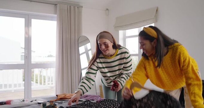 Diverse female friends sorting and comparing clothes on bed, preparing outfits for day out