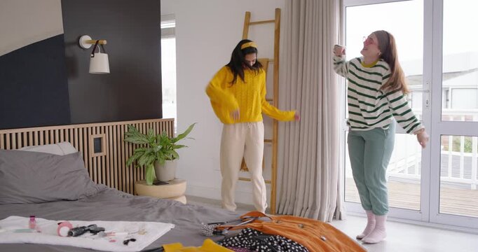 Diverse female friends exchanging looks and dancing, mirroring hops by bed with clothes