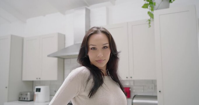 Adult woman responding to camera, posing hands on hips, smiling in home kitchen with range hood