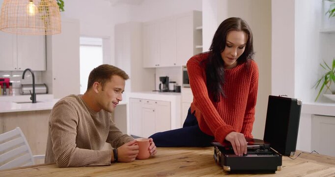 Couple in kitchen, woman holding vinyl, operating turntable, starting playback as man sipping mug