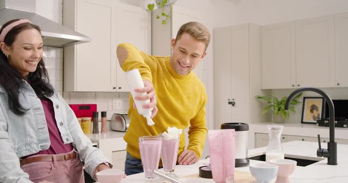 Couple piping whipped cream, blender running, adding cherries, straws, finishing shakes in kitchen