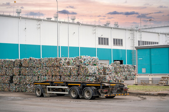 Bales of plastic waste are neatly stacked at a recycling facility during the evening, showcasing efforts to reduce environmental impact and promote sustainability