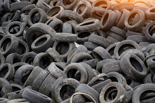 Old tires stacked high in a recycling yard reveal the pressing issue of waste management in urban areas. Sunlight casts a warm glow on the scene