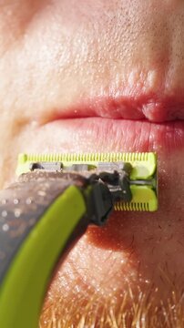 Adult Man Trims Mustache With Electric Razor in Sunlit Close Up, Showing Personal Grooming and Self Care Vertical video.
