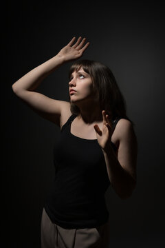 Young woman looking up with hands raised in fear and surprise against a dark background