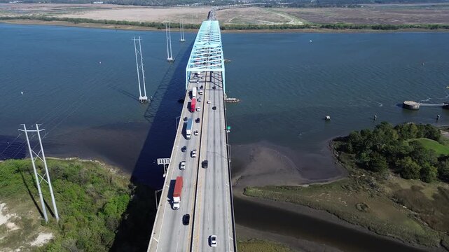 Elevated highway spans guide Interstate 526 across South Carolina Lowcountry marshes toward Cooper River blue steel trusses. High voltage utility pylons stand in water, North Charleston